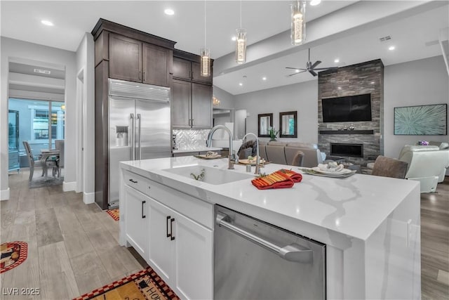 kitchen with dark brown cabinetry, a large fireplace, sink, a kitchen island with sink, and appliances with stainless steel finishes