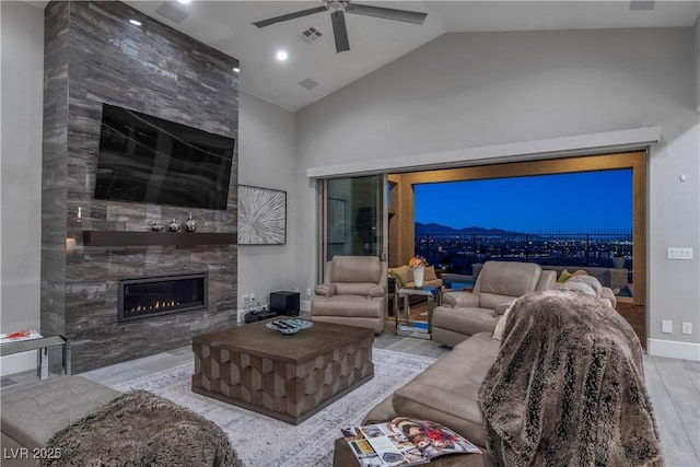 living room with ceiling fan, vaulted ceiling, light wood-type flooring, and a tiled fireplace