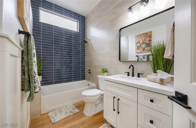 full bathroom with tiled shower / bath combo, toilet, vanity, tile walls, and hardwood / wood-style flooring