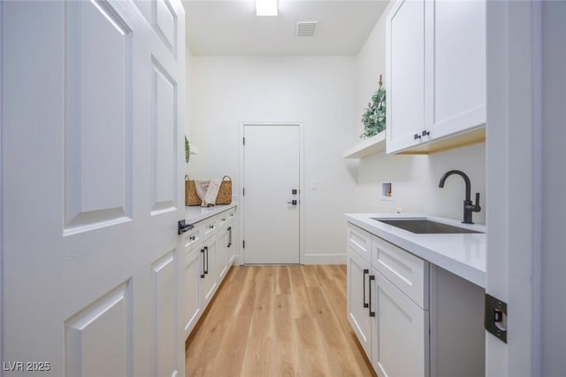 clothes washing area featuring washer hookup, cabinets, sink, and light hardwood / wood-style flooring