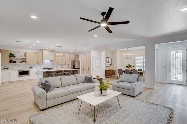 living room with ceiling fan with notable chandelier and light hardwood / wood-style floors