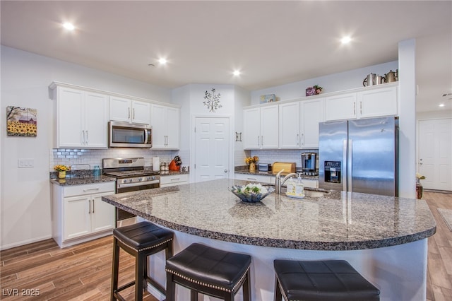 kitchen with a large island with sink, sink, white cabinets, and stainless steel appliances