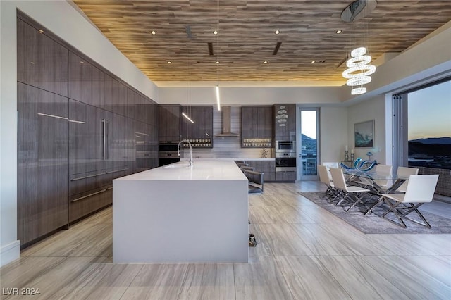 kitchen with wall chimney range hood, sink, hanging light fixtures, a kitchen island, and wood ceiling