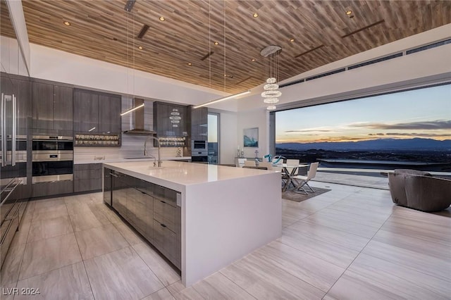 kitchen with pendant lighting, wall chimney exhaust hood, a large island, and wood ceiling