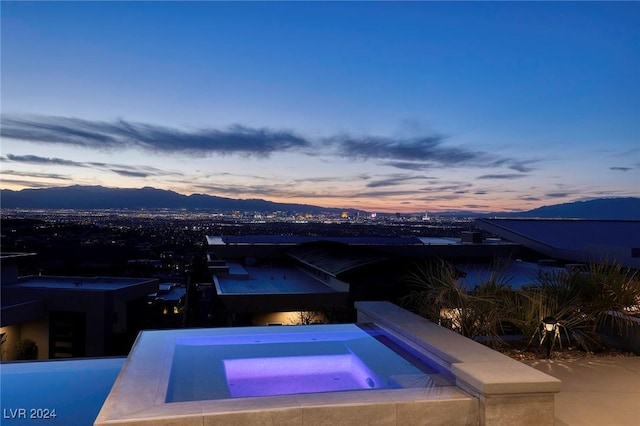 pool at dusk featuring an in ground hot tub and a mountain view