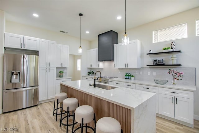 kitchen with stainless steel refrigerator with ice dispenser, a center island with sink, white cabinetry, and sink