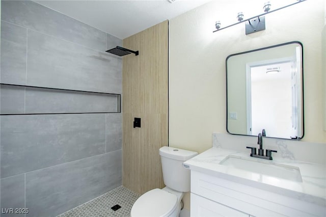 bathroom with a tile shower, vanity, and toilet