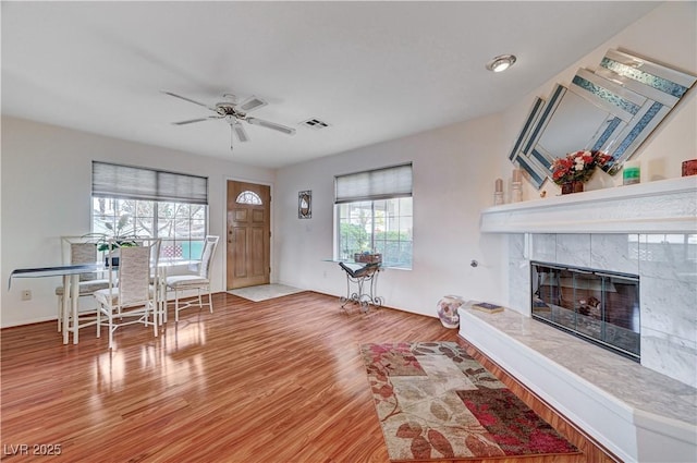 living room featuring a tiled fireplace, ceiling fan, and light hardwood / wood-style flooring