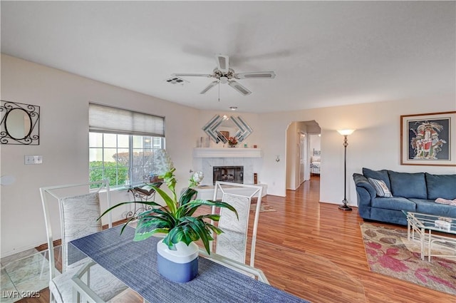 living room with a tiled fireplace, ceiling fan, and light hardwood / wood-style flooring