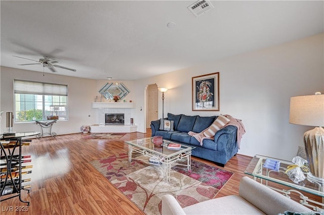 living room featuring a tiled fireplace, ceiling fan, and hardwood / wood-style flooring