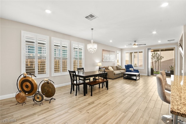 dining room with ceiling fan with notable chandelier and light wood-type flooring