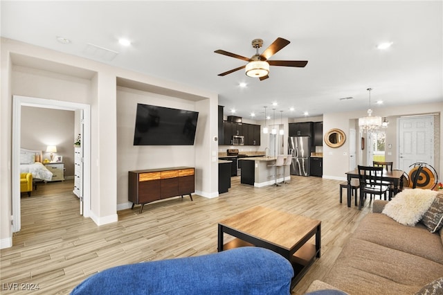 living room featuring ceiling fan with notable chandelier, light hardwood / wood-style floors, and sink