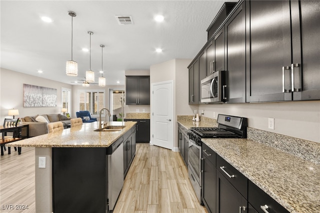 kitchen featuring appliances with stainless steel finishes, light stone counters, sink, pendant lighting, and a center island with sink