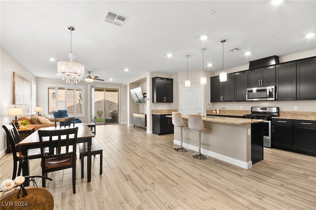 kitchen featuring light stone countertops, a kitchen island with sink, hanging light fixtures, and stainless steel appliances