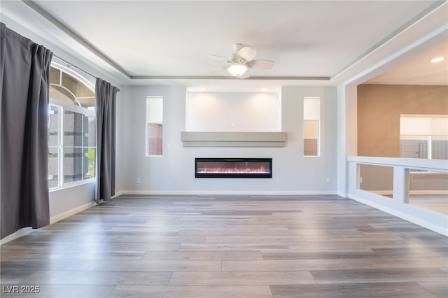 unfurnished living room featuring hardwood / wood-style floors, a tray ceiling, and ceiling fan