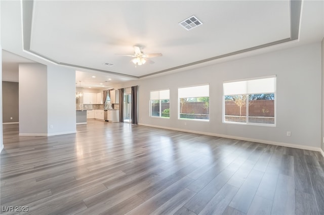 unfurnished living room with hardwood / wood-style floors, ceiling fan with notable chandelier, and a tray ceiling