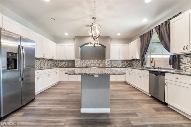 kitchen with a kitchen island, dark stone countertops, pendant lighting, white cabinets, and appliances with stainless steel finishes