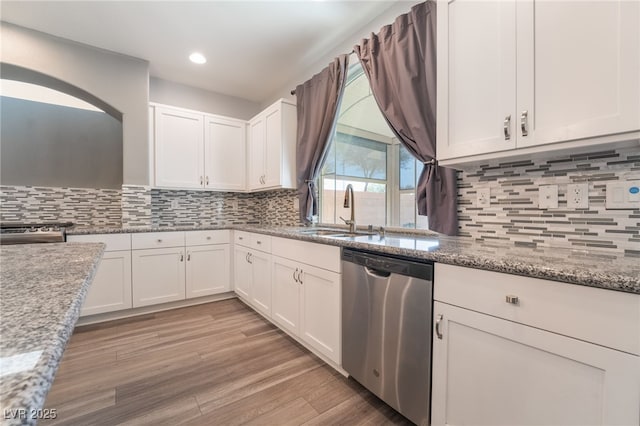 kitchen featuring white cabinets, decorative backsplash, stainless steel dishwasher, and light stone countertops