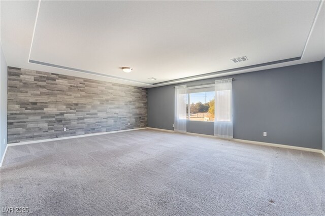 carpeted empty room featuring a tray ceiling and wood walls