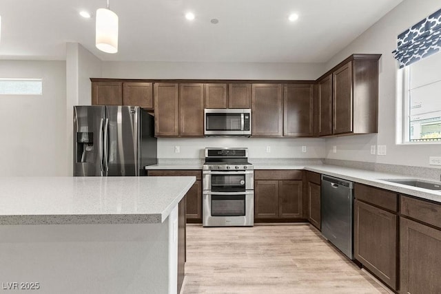 kitchen with sink, stainless steel appliances, pendant lighting, light hardwood / wood-style floors, and dark brown cabinets