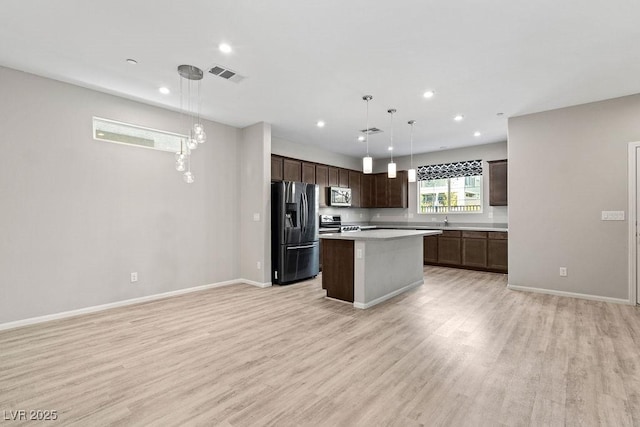 kitchen featuring appliances with stainless steel finishes, light wood-type flooring, decorative light fixtures, and a kitchen island