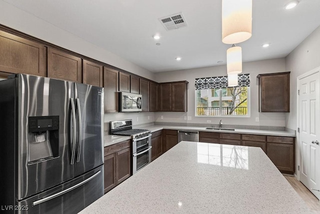 kitchen with light stone counters, dark brown cabinets, stainless steel appliances, sink, and decorative light fixtures