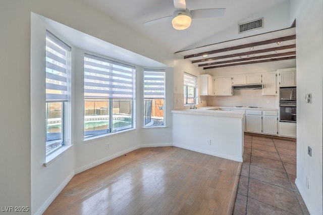 kitchen with tasteful backsplash, beamed ceiling, kitchen peninsula, oven, and white cabinets