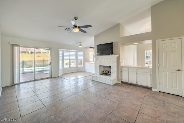 unfurnished living room with ceiling fan, light tile patterned floors, lofted ceiling, and a brick fireplace