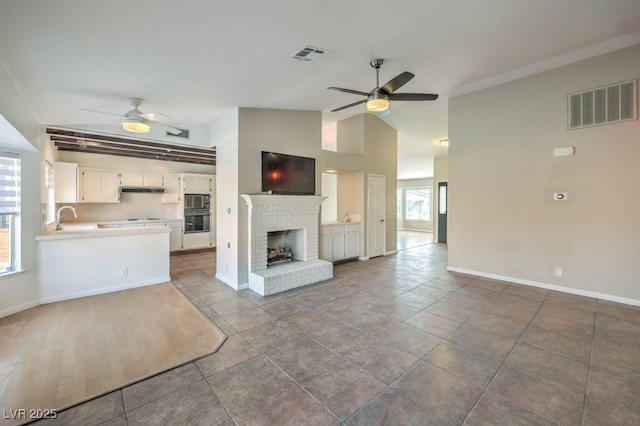 unfurnished living room featuring a brick fireplace, ceiling fan, sink, tile patterned flooring, and lofted ceiling