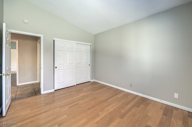 unfurnished bedroom featuring light hardwood / wood-style floors, lofted ceiling, and a closet