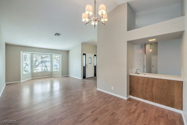 unfurnished living room featuring sink, a chandelier, lofted ceiling, and light wood-type flooring