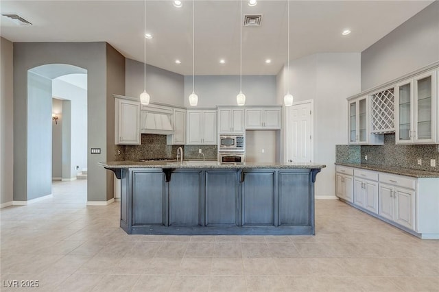 kitchen featuring hanging light fixtures, dark stone countertops, a towering ceiling, white cabinetry, and stainless steel appliances