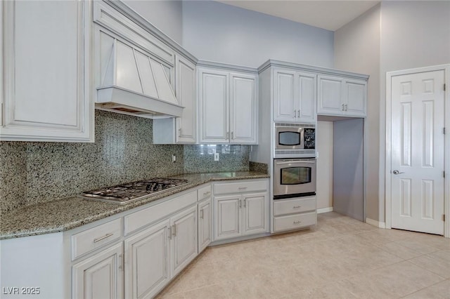 kitchen featuring white cabinets, custom range hood, stainless steel appliances, and light stone countertops