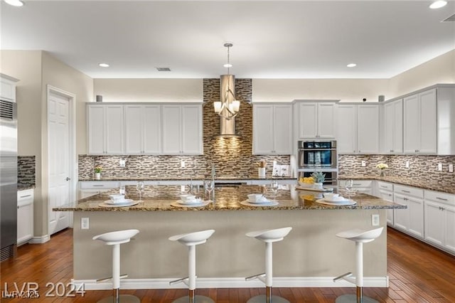 kitchen featuring a kitchen bar, hanging light fixtures, a center island with sink, and stainless steel appliances