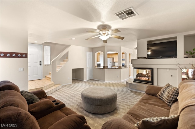 living room with a textured ceiling, light colored carpet, ceiling fan, and a tiled fireplace