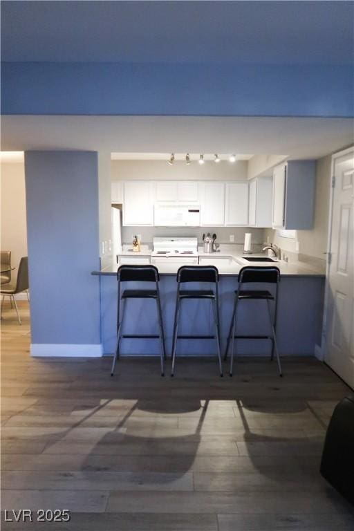 kitchen with a kitchen bar, white cabinetry, dark hardwood / wood-style floors, and white appliances