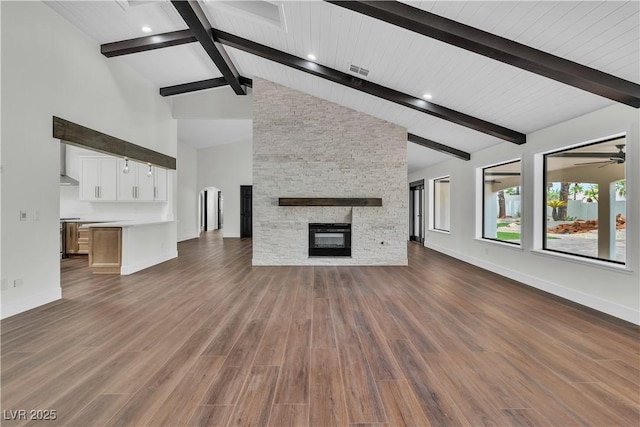 unfurnished living room with ceiling fan, dark wood-type flooring, a stone fireplace, beamed ceiling, and high vaulted ceiling