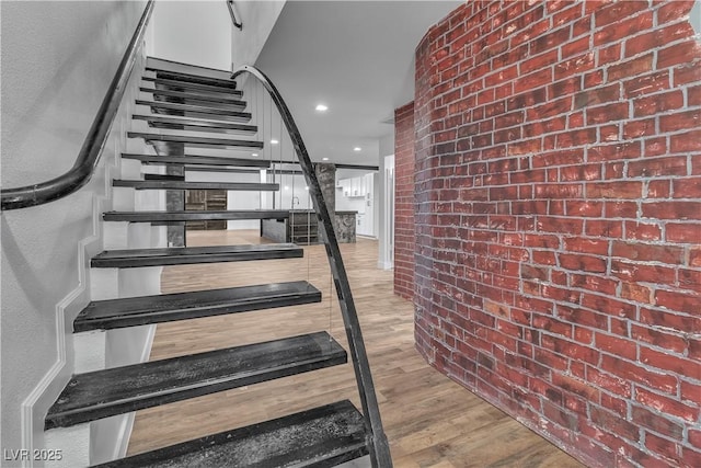 stairs with wood-type flooring and brick wall