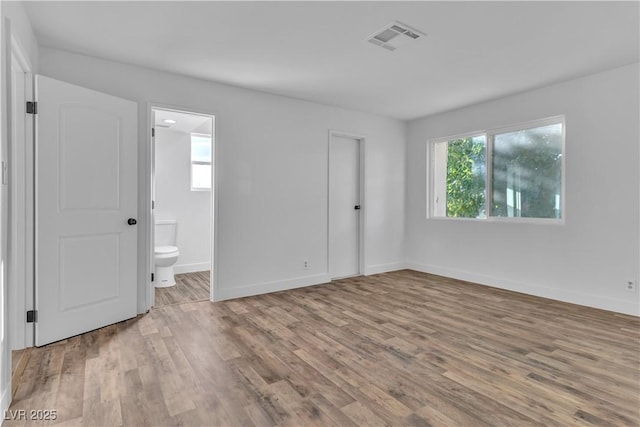 unfurnished bedroom featuring light wood-type flooring, ensuite bath, and a closet