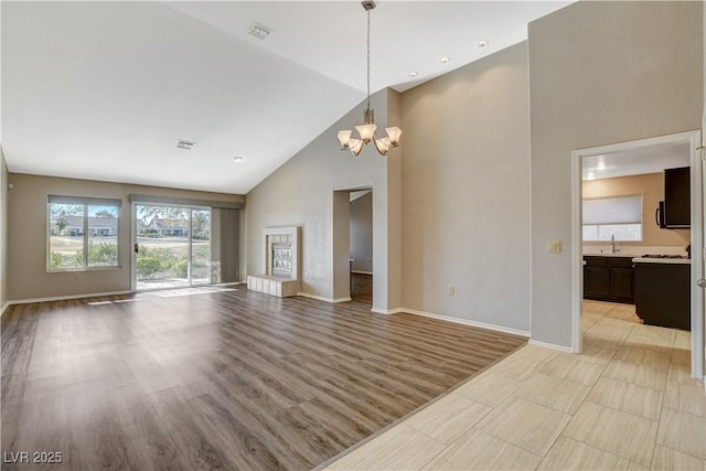 unfurnished living room featuring an inviting chandelier, high vaulted ceiling, and light hardwood / wood-style floors