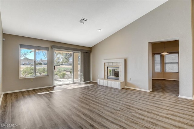 unfurnished living room with hardwood / wood-style flooring, lofted ceiling, and a tiled fireplace