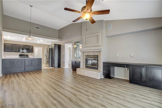 unfurnished living room featuring light hardwood / wood-style floors, ceiling fan, a tiled fireplace, and vaulted ceiling