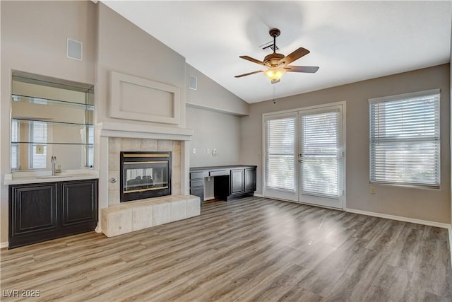 unfurnished living room featuring lofted ceiling, sink, light wood-type flooring, ceiling fan, and a fireplace