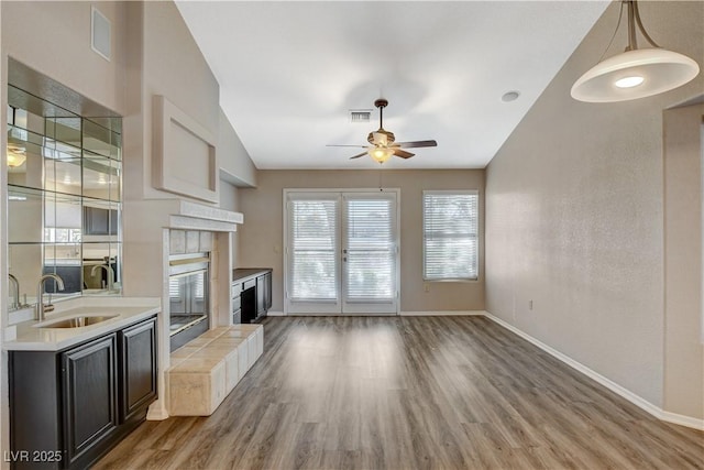 unfurnished living room with a tiled fireplace, sink, hardwood / wood-style floors, and ceiling fan