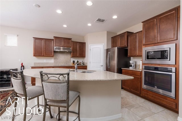 kitchen featuring a kitchen island with sink, sink, light stone countertops, light tile patterned floors, and appliances with stainless steel finishes