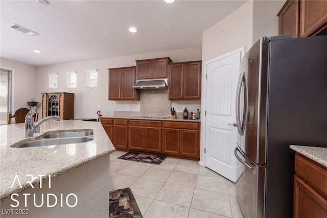 kitchen with sink, light stone countertops, tasteful backsplash, light tile patterned flooring, and stainless steel refrigerator