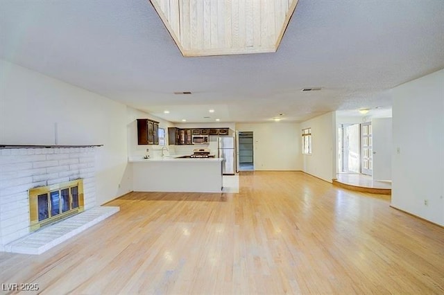 unfurnished living room with a textured ceiling, light hardwood / wood-style flooring, a brick fireplace, and sink