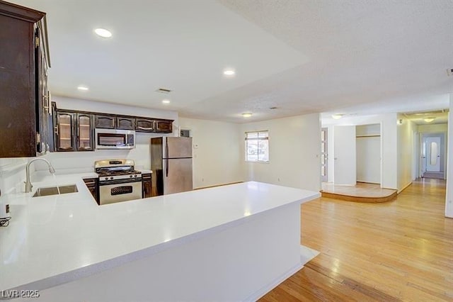 kitchen featuring dark brown cabinetry, sink, stainless steel appliances, kitchen peninsula, and light wood-type flooring