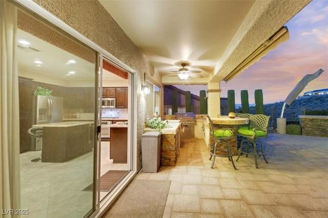 patio terrace at dusk featuring ceiling fan, area for grilling, and grilling area