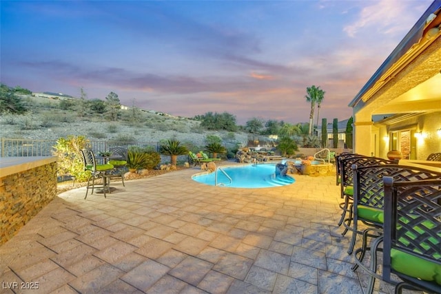 pool at dusk with pool water feature, a patio, and a hot tub